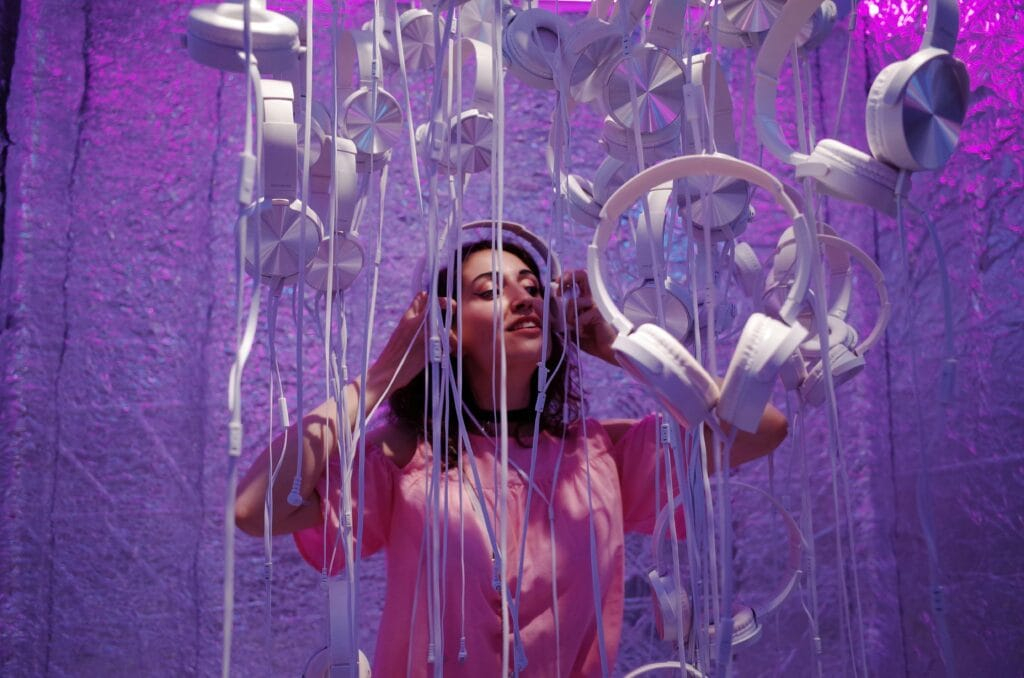 Photo of Woman Wearing Pink Shirt Standing Near White Headphones Against Purple Background