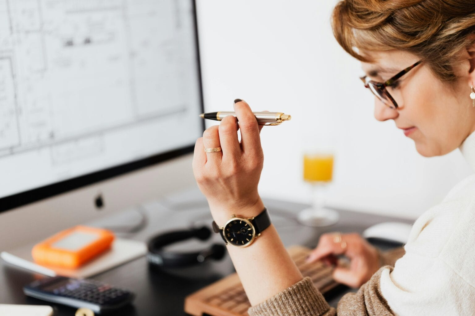 Side view of crop focused businesswoman in eyeglasses with pen in hand making report of financial results while working on computer